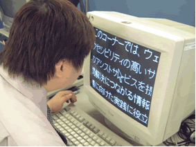 パソコンのモニターに、黒い背景に白く表示された大きな字を見ている人の写真